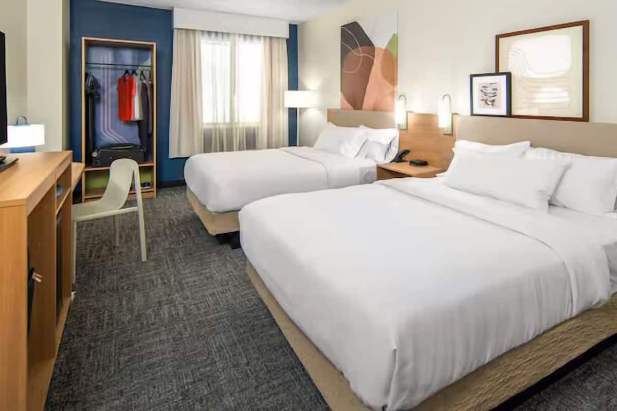 A hotel room with two beds, a desk, a chair, a wardrobe, and a window with curtains.