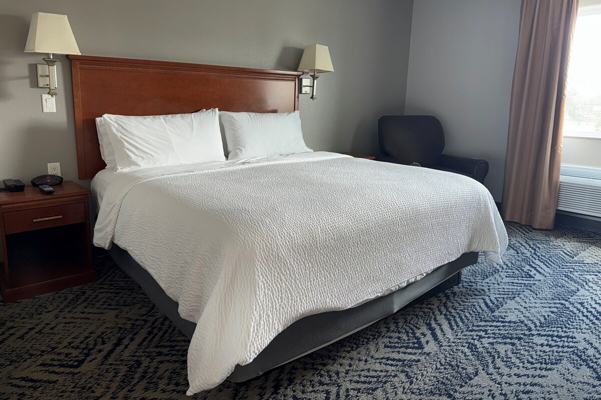 A hotel room with a large bed, two bedside lamps, a chair, and a carpeted floor.