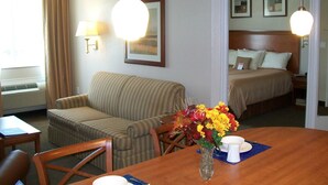 A hotel room with a bed, a sofa, a dining table with a vase of flowers, and a lamp. - Candlewood Suites La Porte by IHG (La Porte)