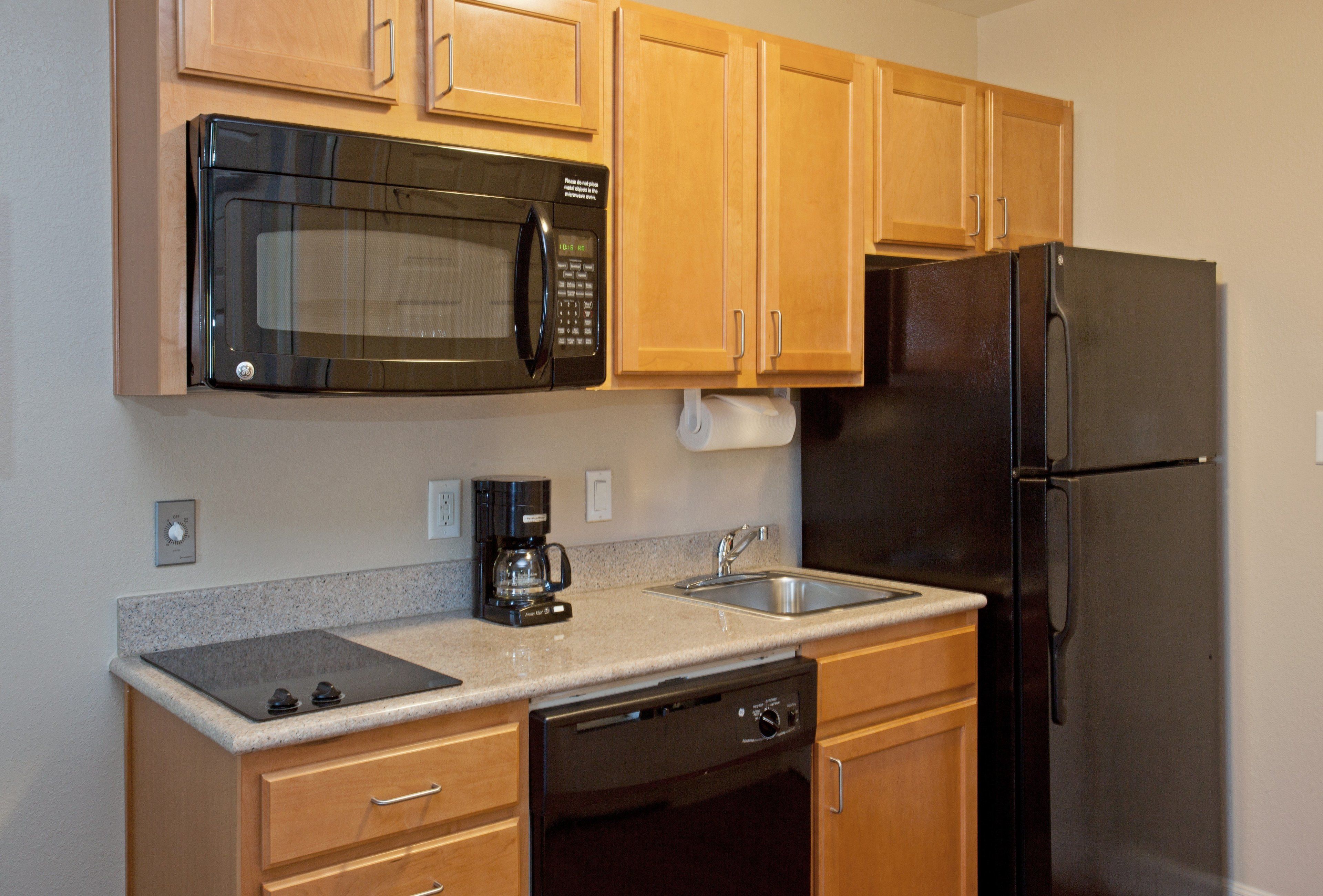 A kitchen with wooden cabinets, a stainless steel refrigerator, a microwave, a dishwasher, and a coffee maker.