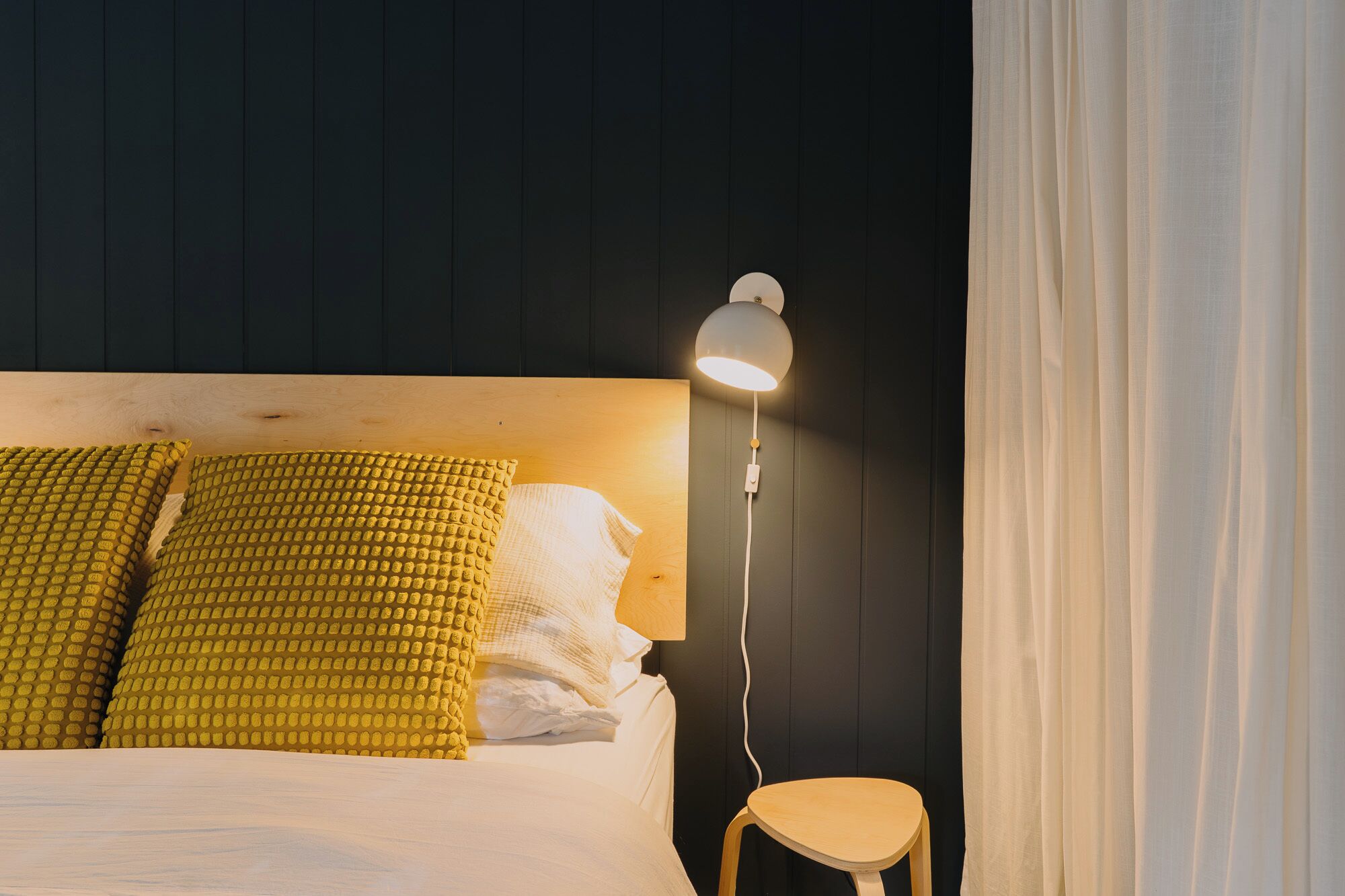A bed with a wooden headboard, a bedside lamp, and a small stool.