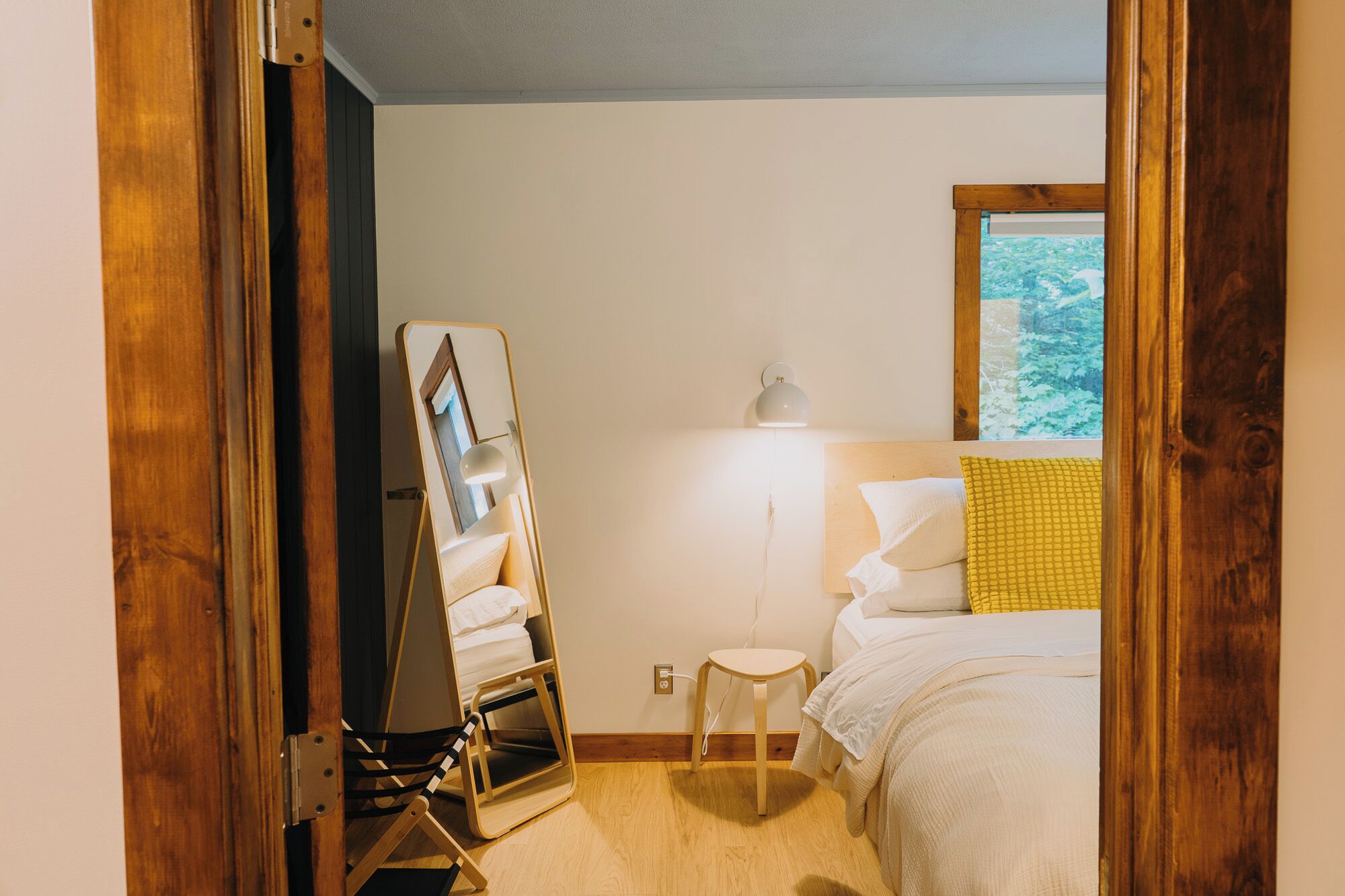 Ein Schlafzimmer mit Bett, Nachttisch, Lampe, Spiegel und Fenster mit Aussicht.