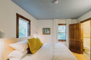 A bedroom with a bed, a window, a door, and a ceiling light.