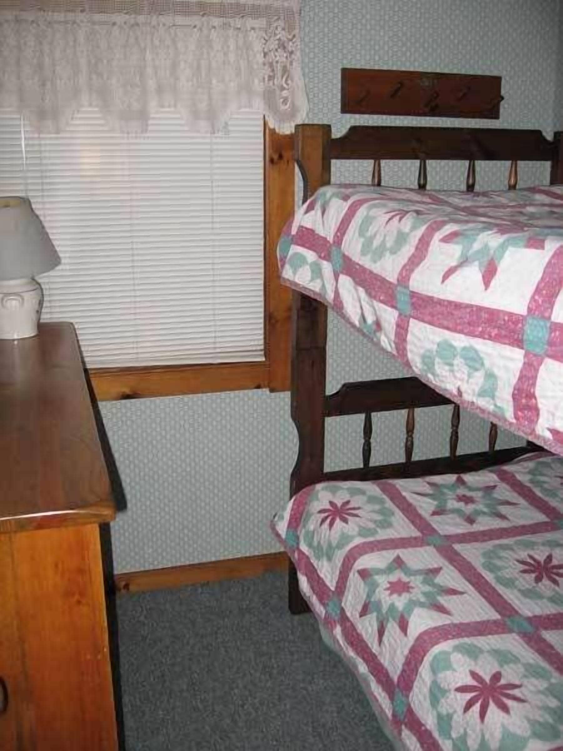 Een stapelbed met een bloemenquilt, een houten hoofdbord en een nachtkastje met een lamp.