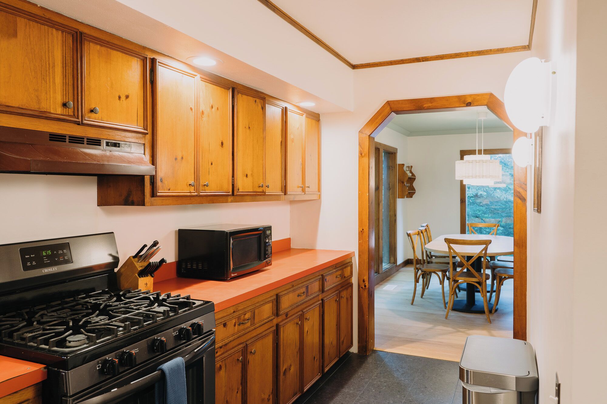 A kitchen with wooden cabinets, a stove, a microwave, and a dining area with a table and chairs.