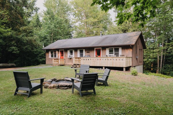 A wooden cabin with a porch, outdoor seating, and a fire pit.