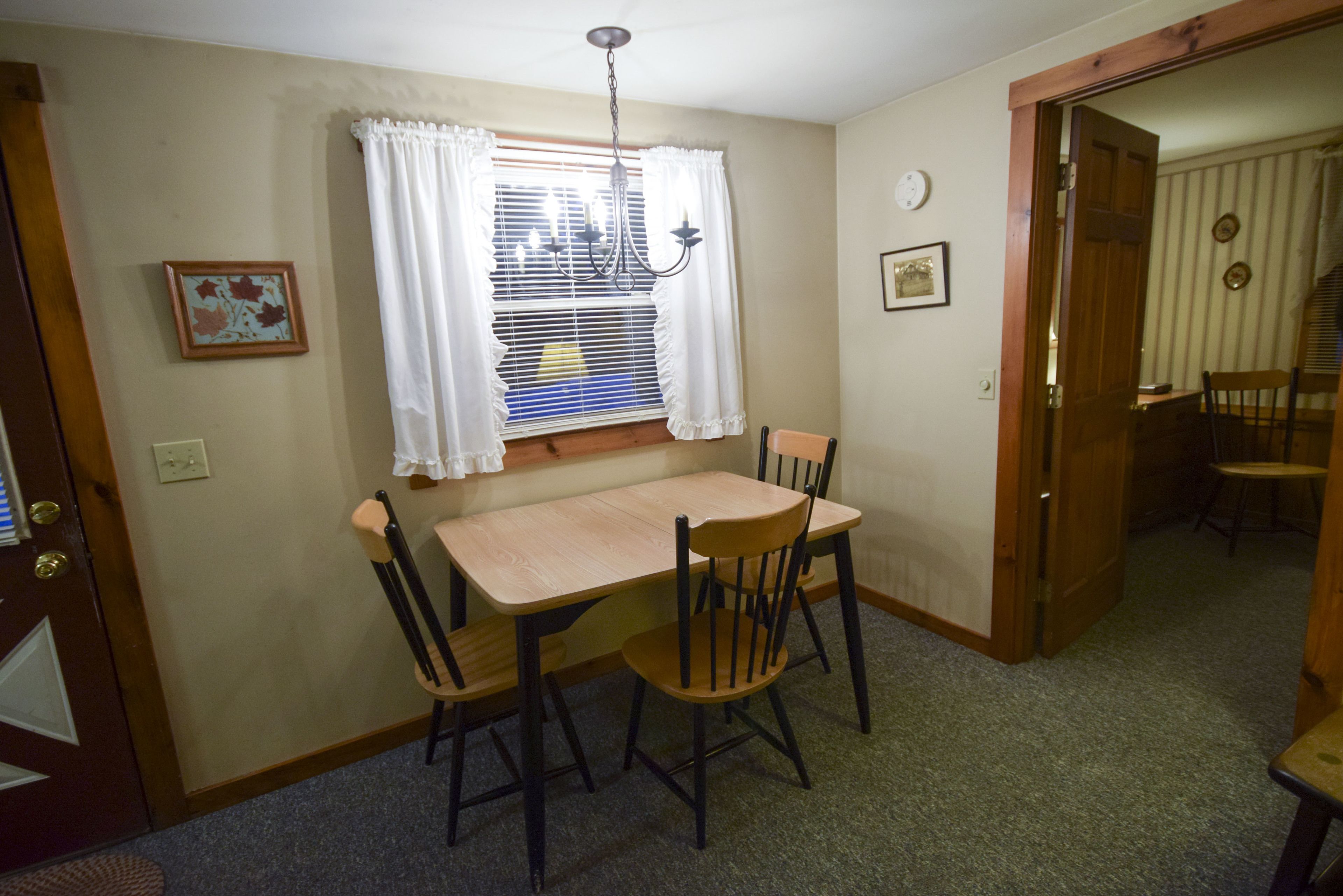 Un comedor con una mesa y sillas de madera, un candelabro y un ventanal con cortinas.