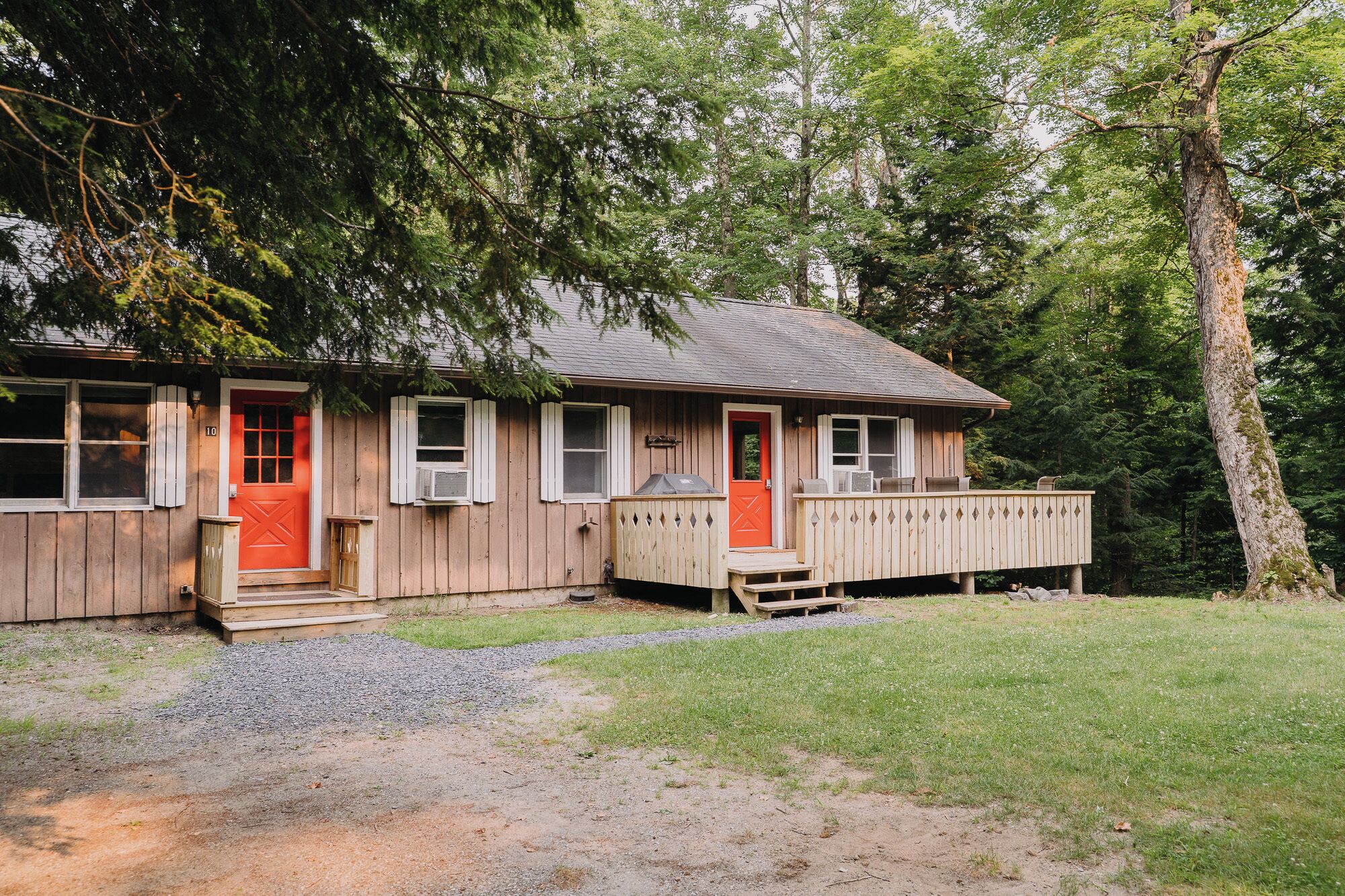A wooden cabin with a red door, a covered porch, and a gravel driveway.