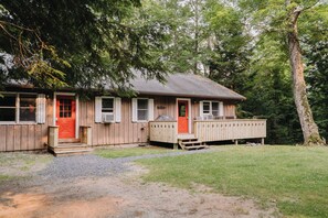 A wooden cabin with a red door, a covered porch, and a gravel driveway.
