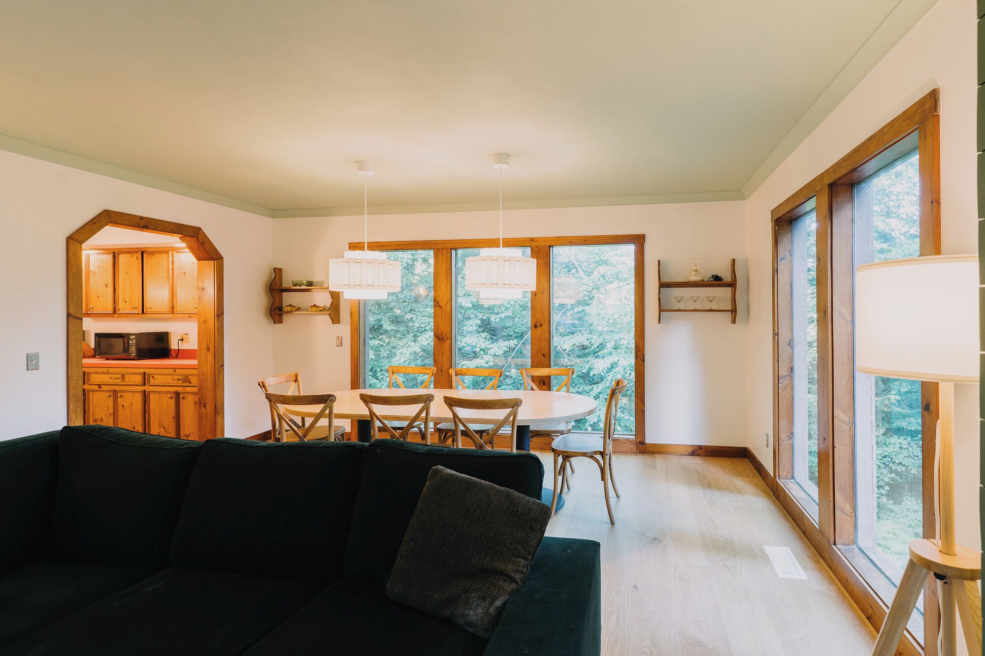 Una sala de estar acogedora con un sofá verde oscuro y una zona de comedor con sillas de madera y una mesa blanca.