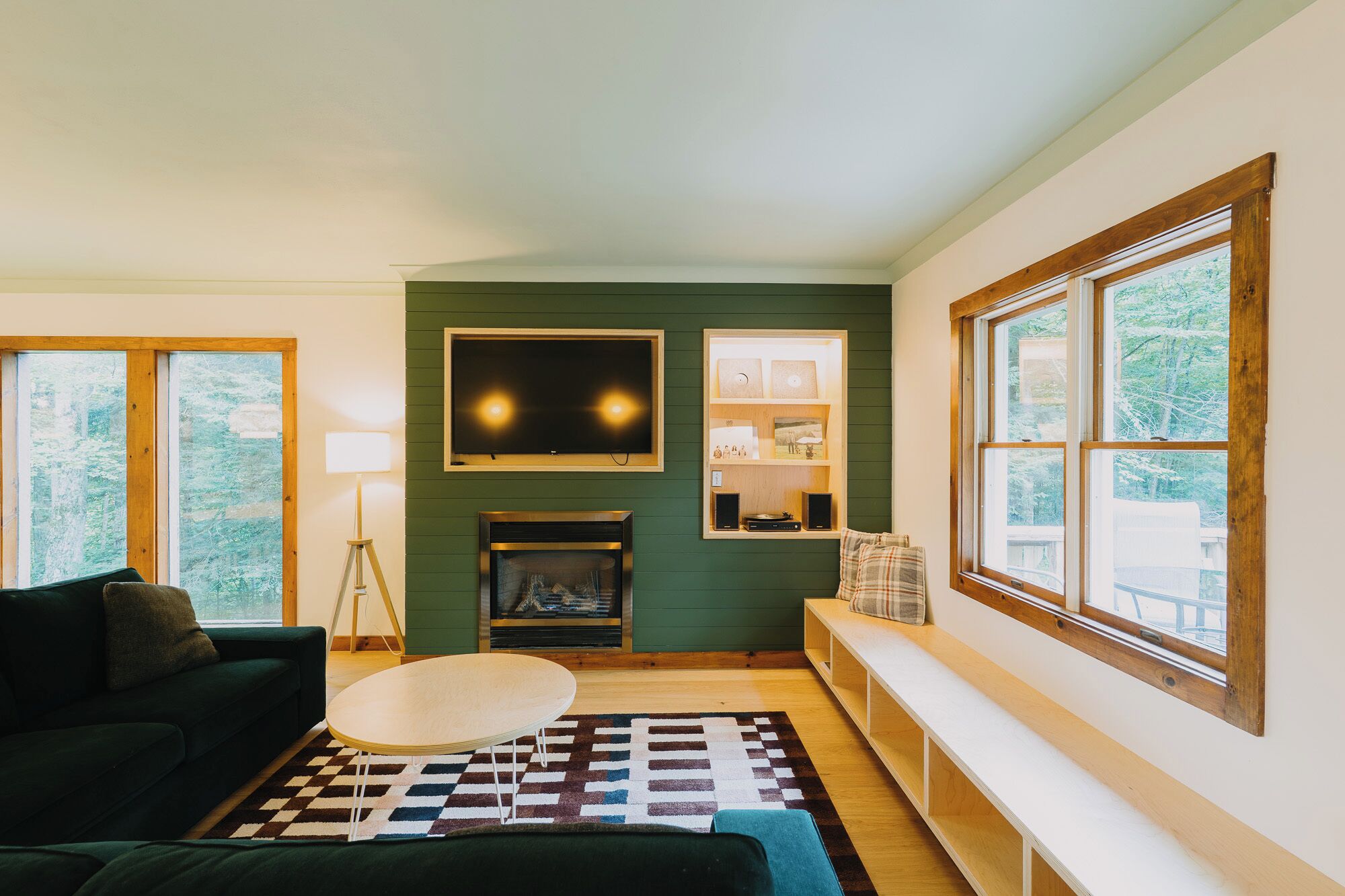 A living room with a fireplace, a sofa, a coffee table, and a large window with a view of trees.