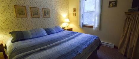 Un dormitorio con cama, mesita de noche, ventana con cortinas y papel tapiz floral.