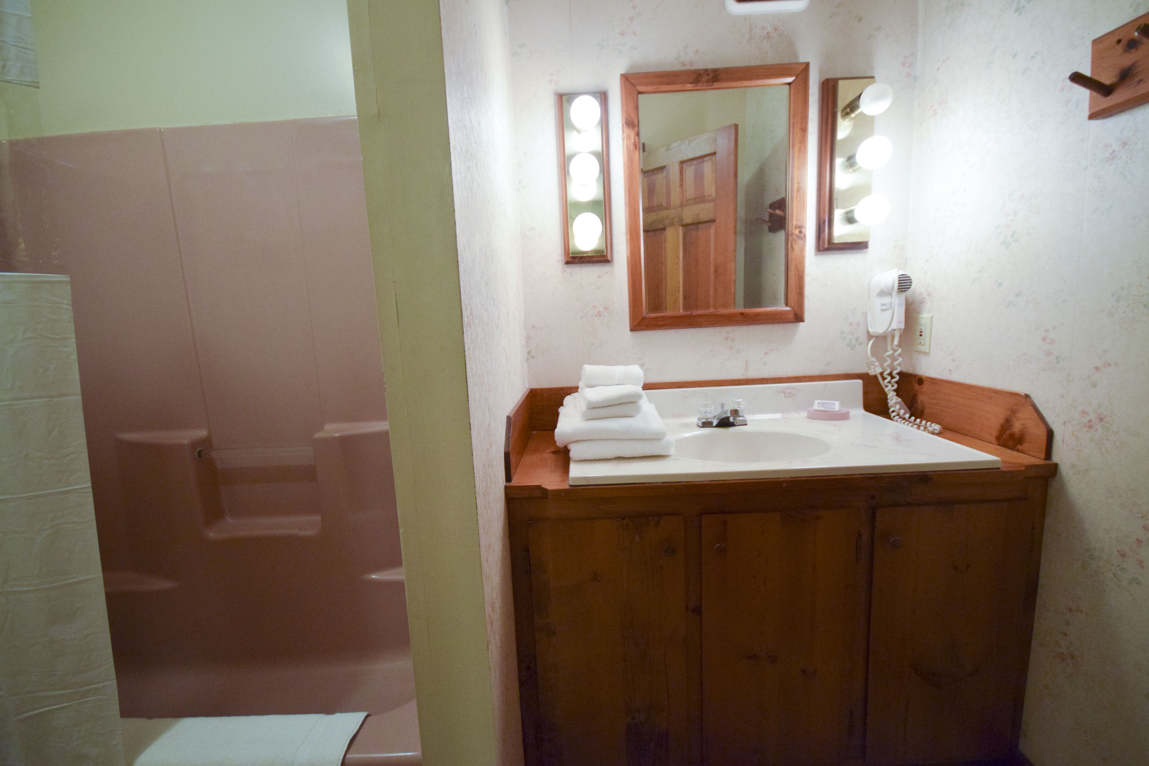 Ein Badezimmer mit einem Holzbadezimmerhocker, einem Waschbecken und einem beleuchteten Spiegel.