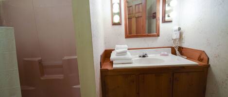Ein Badezimmer mit einem Holzbadezimmerhocker, einem Waschbecken und einem beleuchteten Spiegel.