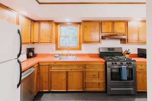 A kitchen with wooden cabinets, a stainless steel stove, and a window. - Stowe Cabins in the Woods (Waterbury Center)