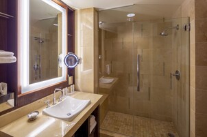 Un baño moderno con ducha de vidrio, un espejo grande y un mueble de tocador color crema.
