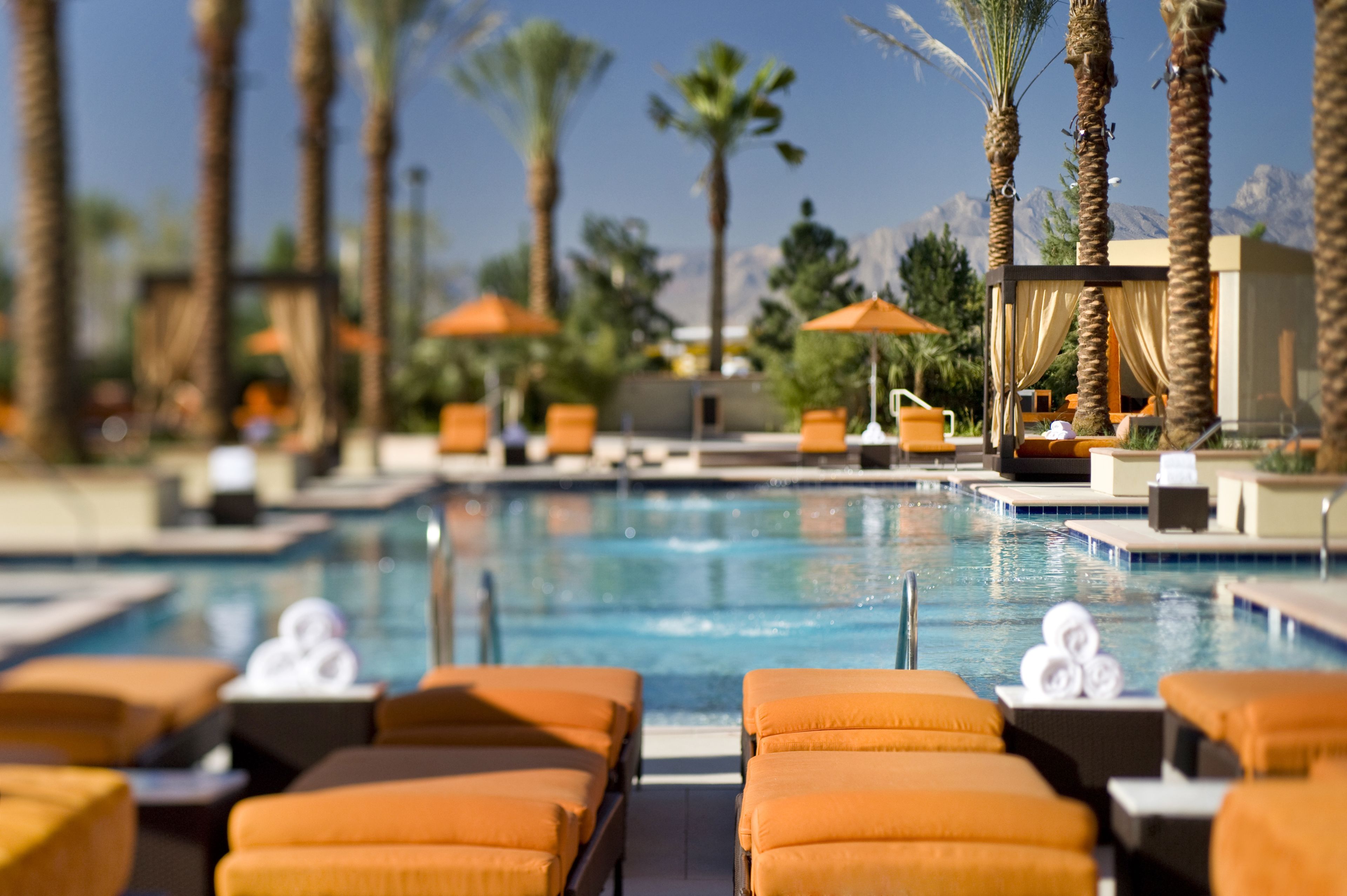 A pool area with lounge chairs, umbrellas, and a view of mountains.