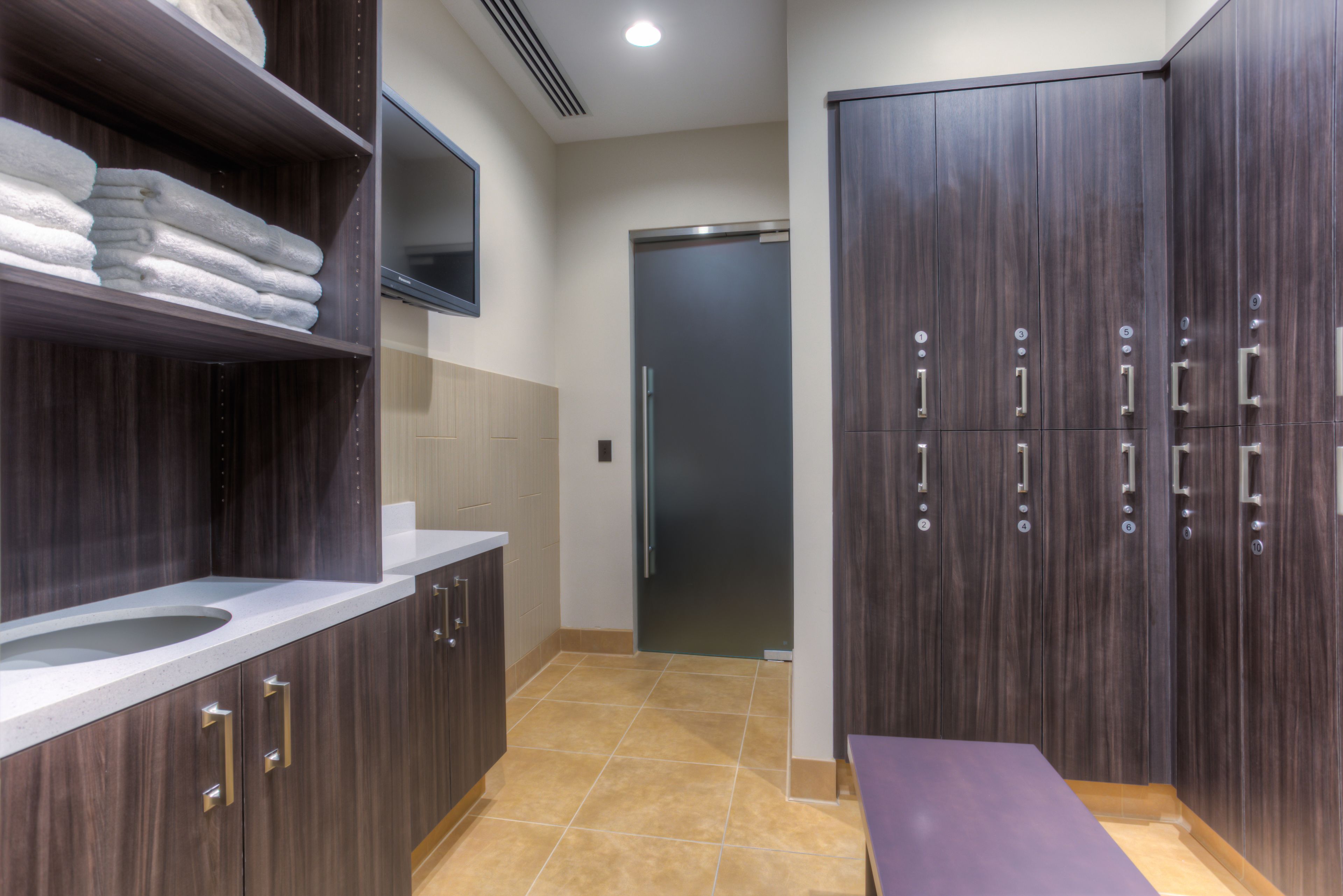 A modern bathroom with dark wood cabinets, a white sink, and a bench.
