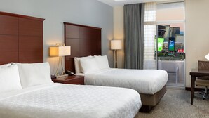 A hotel room with two beds, a desk, and a view of a cityscape through a large window.