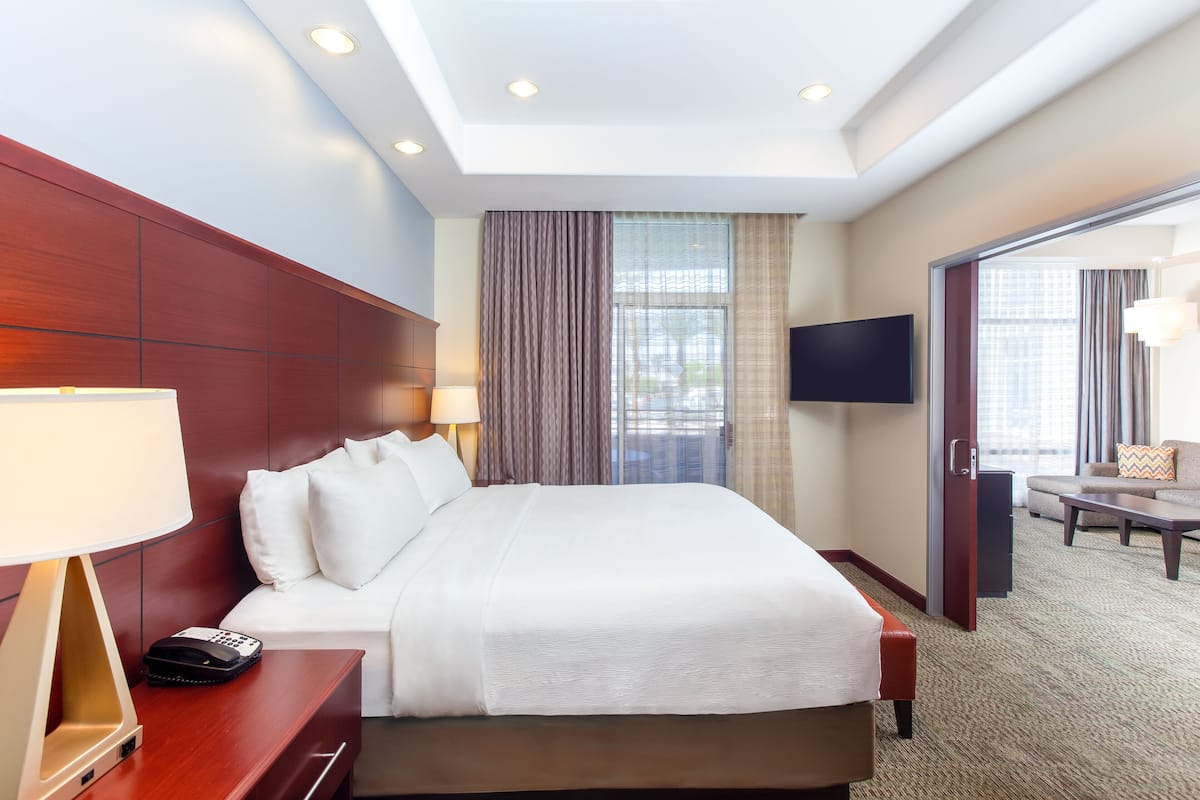 A hotel room with a large bed, bedside lamps, a TV, a sofa, and a view of the outdoors.