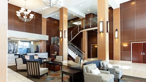 A spacious lobby with a central staircase, multiple seating areas, and a visible kitchen area.