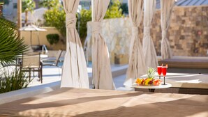 A sunlit outdoor seating area with a table set for two, featuring a fruit platter and two drinks.
