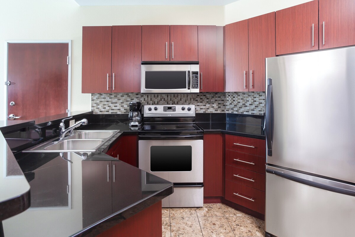 A modern kitchen with stainless steel appliances, wooden cabinets, and a black countertop.