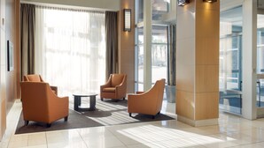 A modern lobby with three brown armchairs, a small round table, and large windows with sheer curtains.