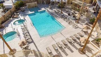 A pool area with multiple lounge chairs and umbrellas, a smaller circular pool, and a stone wall.