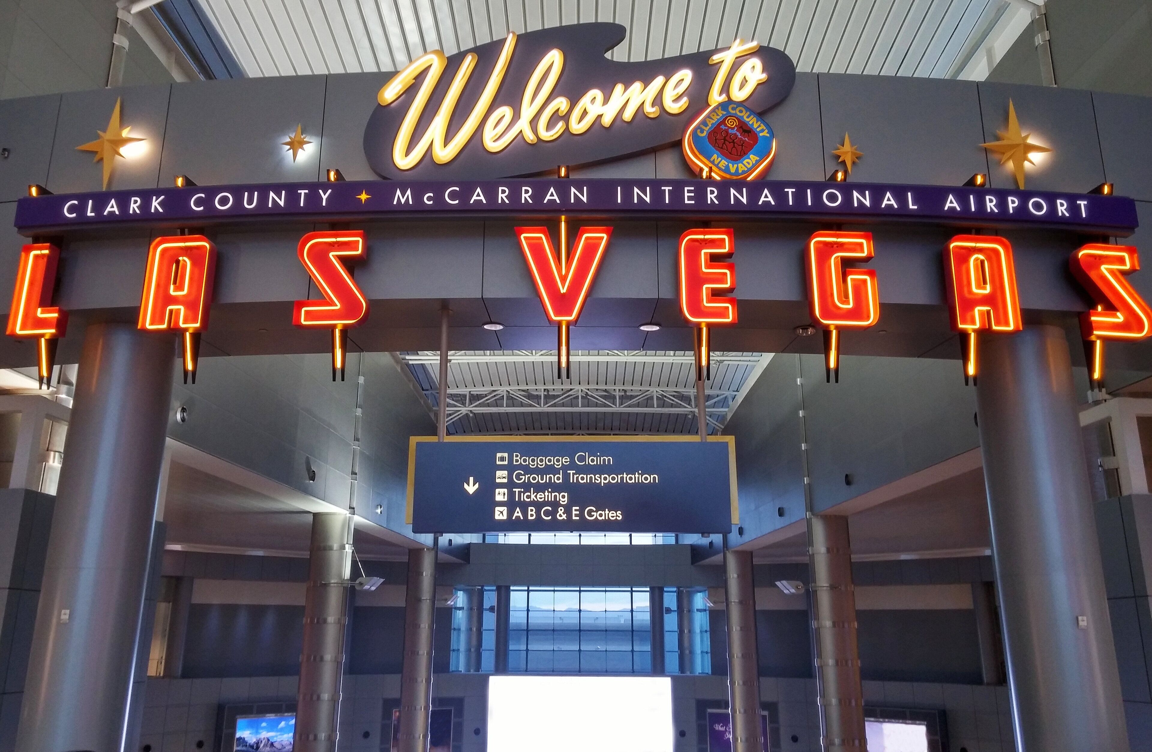 Ein Schild am Eingang eines Flughafens mit der Aufschrift 'Welcome to Las Vegas' und Wegweisern zu Gepäckausgabe, Bodenverkehrsdienst, Ticketverkauf und zu den Gates.