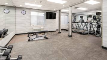 Un gimnasio con cintas de correr, mancuernas y un banco.