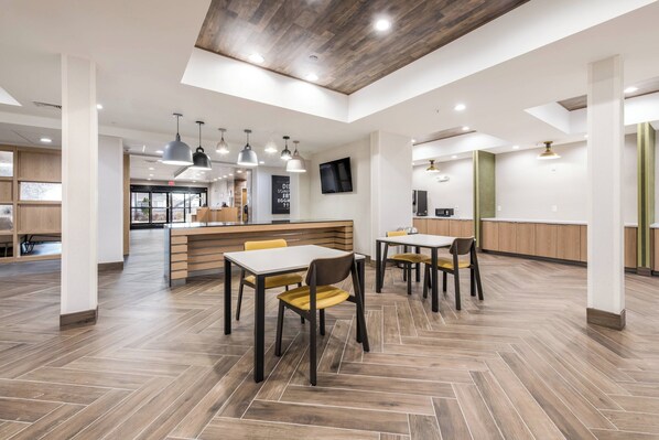 Un grand espace intérieur doté d’un plancher en bois, de plusieurs tables et chaises, et d’une cuisine moderne en arrière-plan.