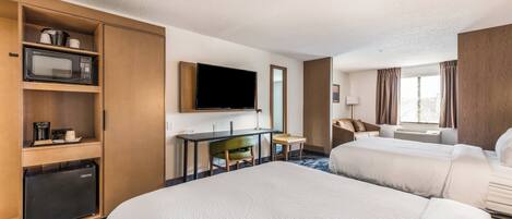 Habitación de hotel con dos camas, un escritorio con silla, televisor, microondas y refrigerador pequeño.