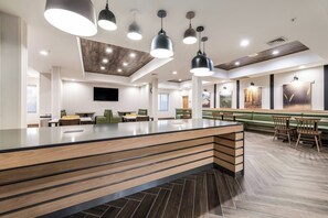 A modern restaurant with a central island, multiple hanging pendant lights, and a herringbone floor pattern. - Fairfield Inn & Suites by Marriott Greensboro Coliseum Area (Greensboro)