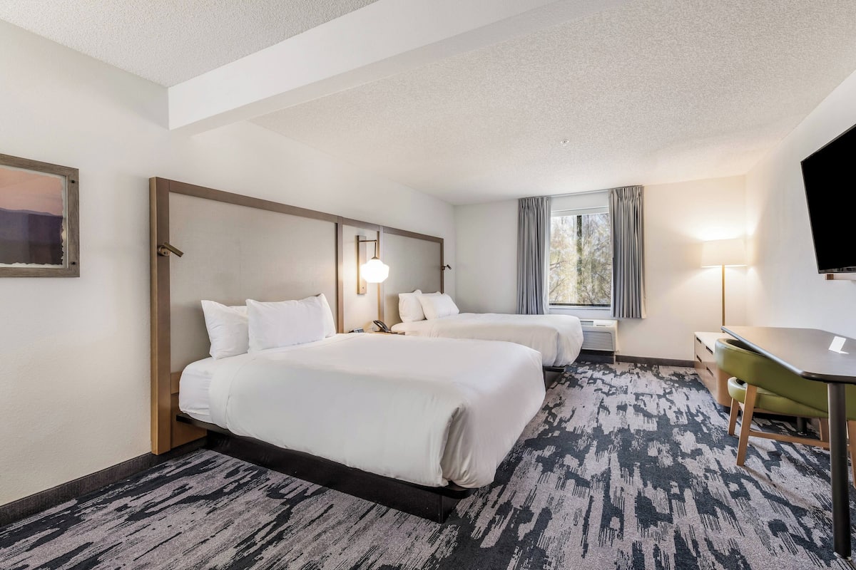 A hotel room with two beds, a desk, a TV, and a window with curtains.