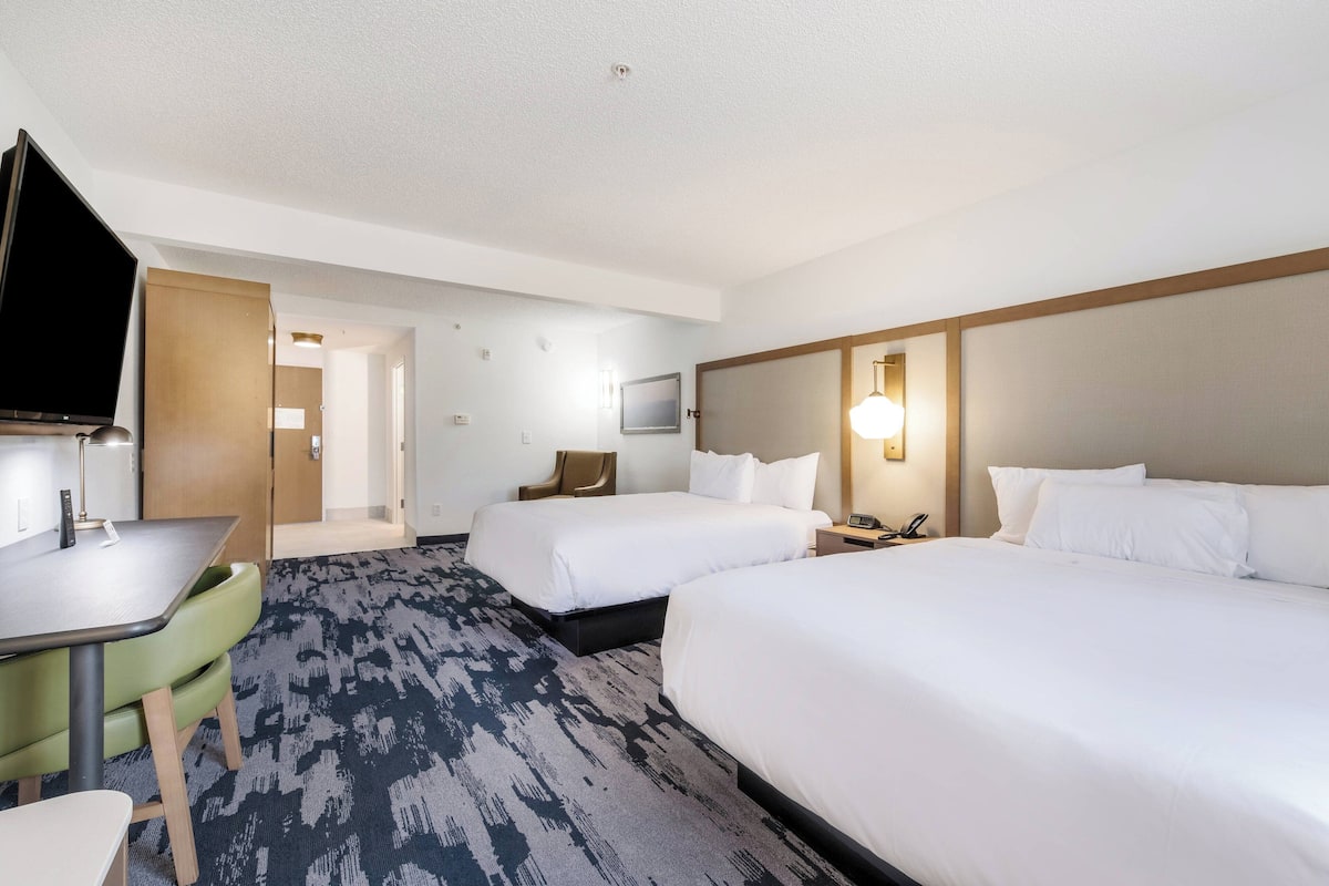 A hotel room with two beds, a desk, a chair, a TV, and a carpeted floor.