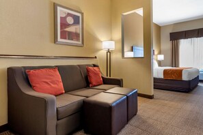 A hotel room with a sofa, a bed, a mirror, and a painting on the wall. - Comfort Suites Airport South (Montgomery)