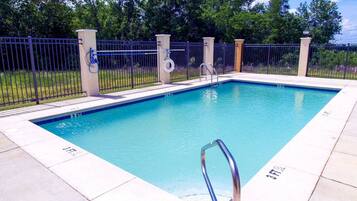 A rectangular swimming pool with a metal ladder and a fence surrounding it.