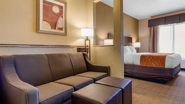 A hotel room with a sofa, a bed, a mirror, and a painting on the wall.