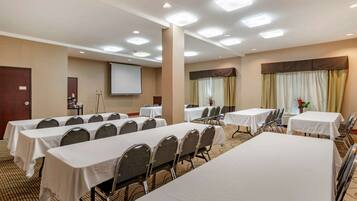 Una sala de conferencias con varias mesas y sillas, una pantalla de proyector y suelo alfombrado.