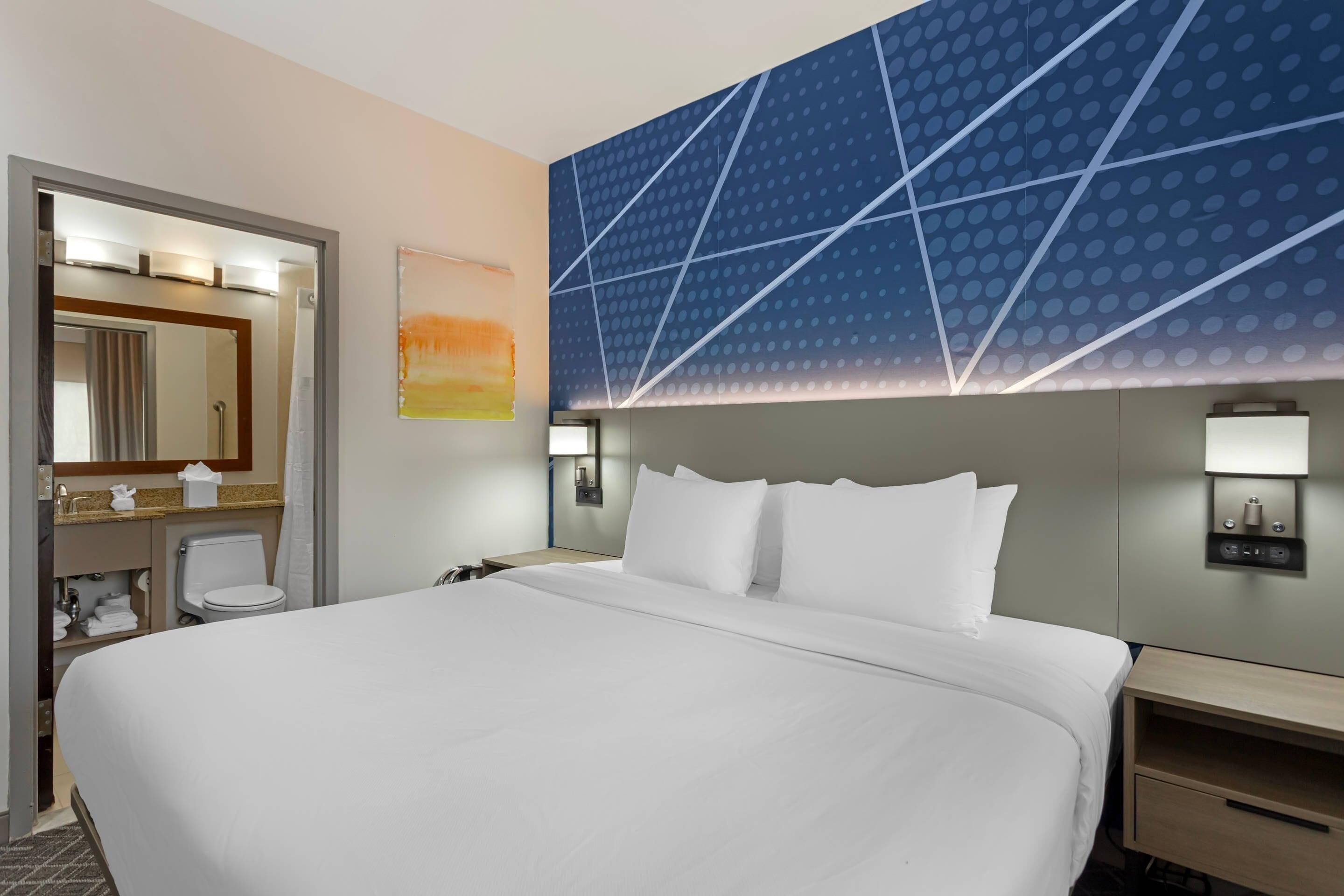 Quarto de hotel com uma cama grande, banheiro com espelho e parede com padrão geométrico.