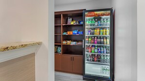 A vending machine stocked with various beverages and snacks, adjacent to a wooden cabinet with shelves. - Comfort Inn Staten Island (Staten Island)