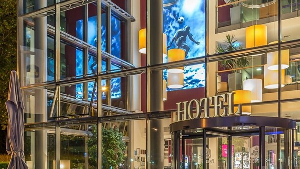 A hotel entrance with a glass facade, outdoor seating area, and a revolving door. - Best Western Premier Hotel Regensburg (Regensburg)