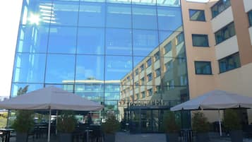 A hotel with a glass facade, outdoor seating, and a clear view of the surrounding buildings.