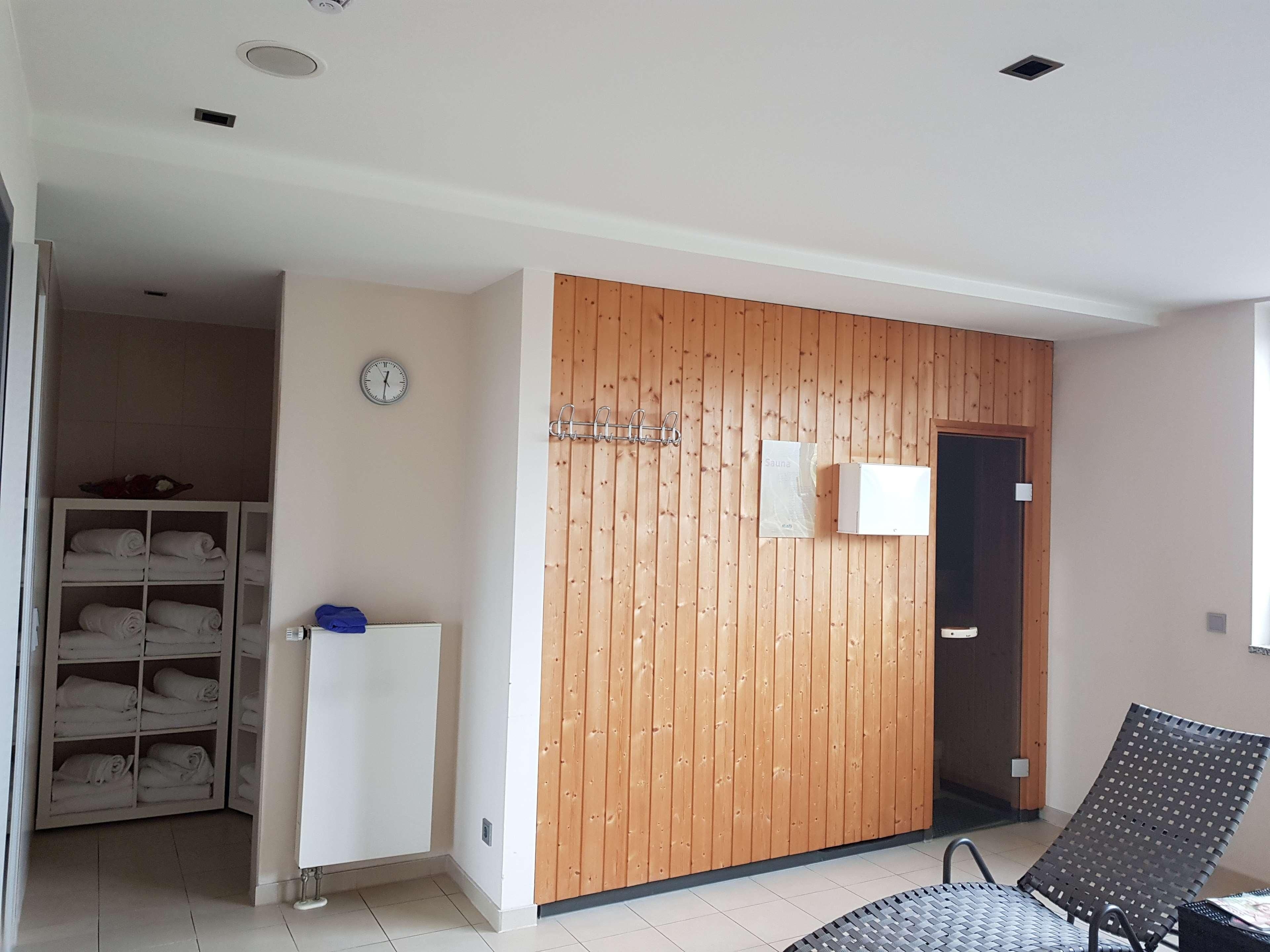Una habitación con un panel de madera en la pared, un armario blanco con toallas, un reloj y una silla.