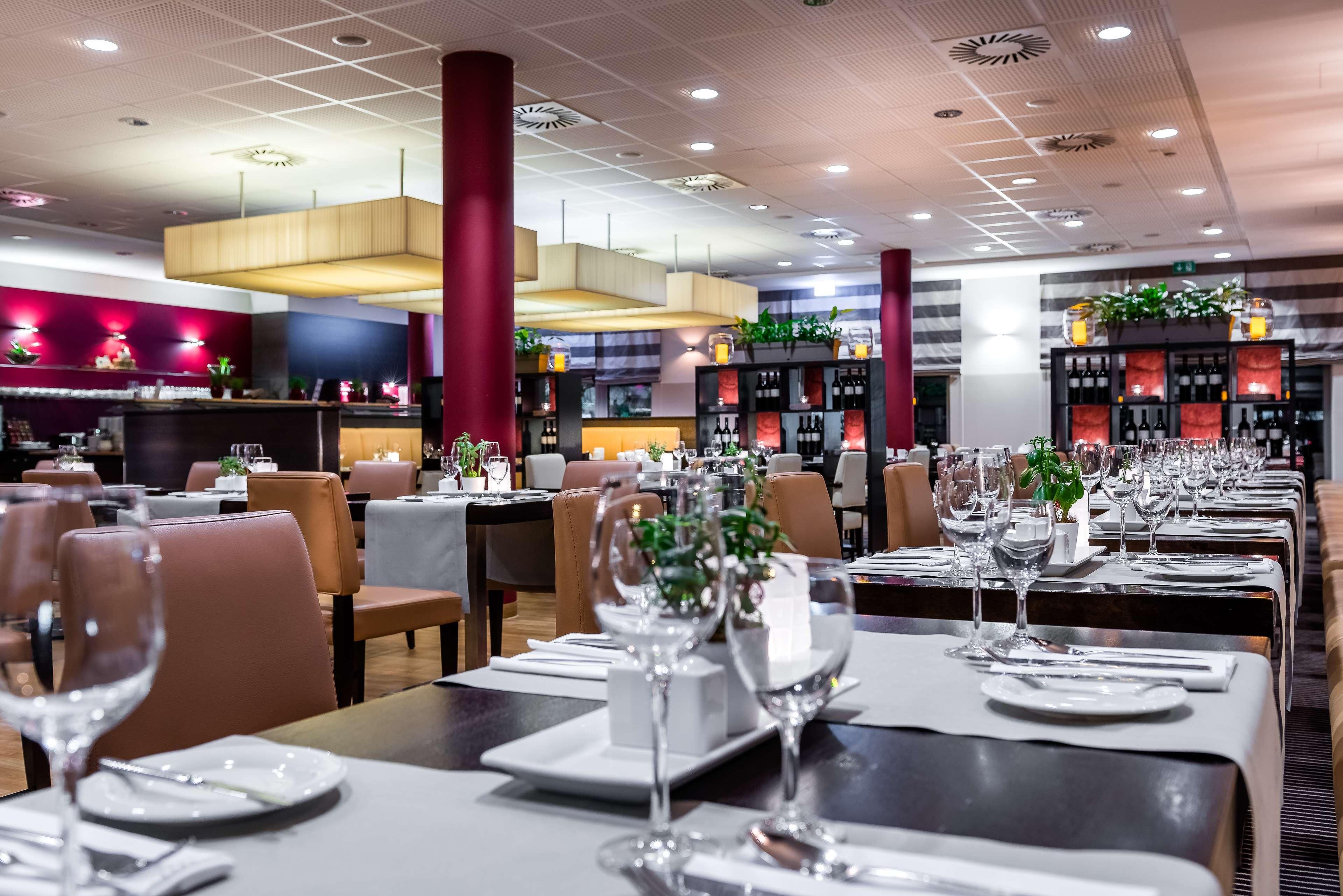 Ein Restaurantinneres mit gedeckten Tischen, einer Bar und einer Decke mit eingelassener Beleuchtung.