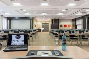 A conference room with rows of tables and chairs, a podium, and a laptop on a table. - Four Points by Sheraton Regensburg (Regensburg)