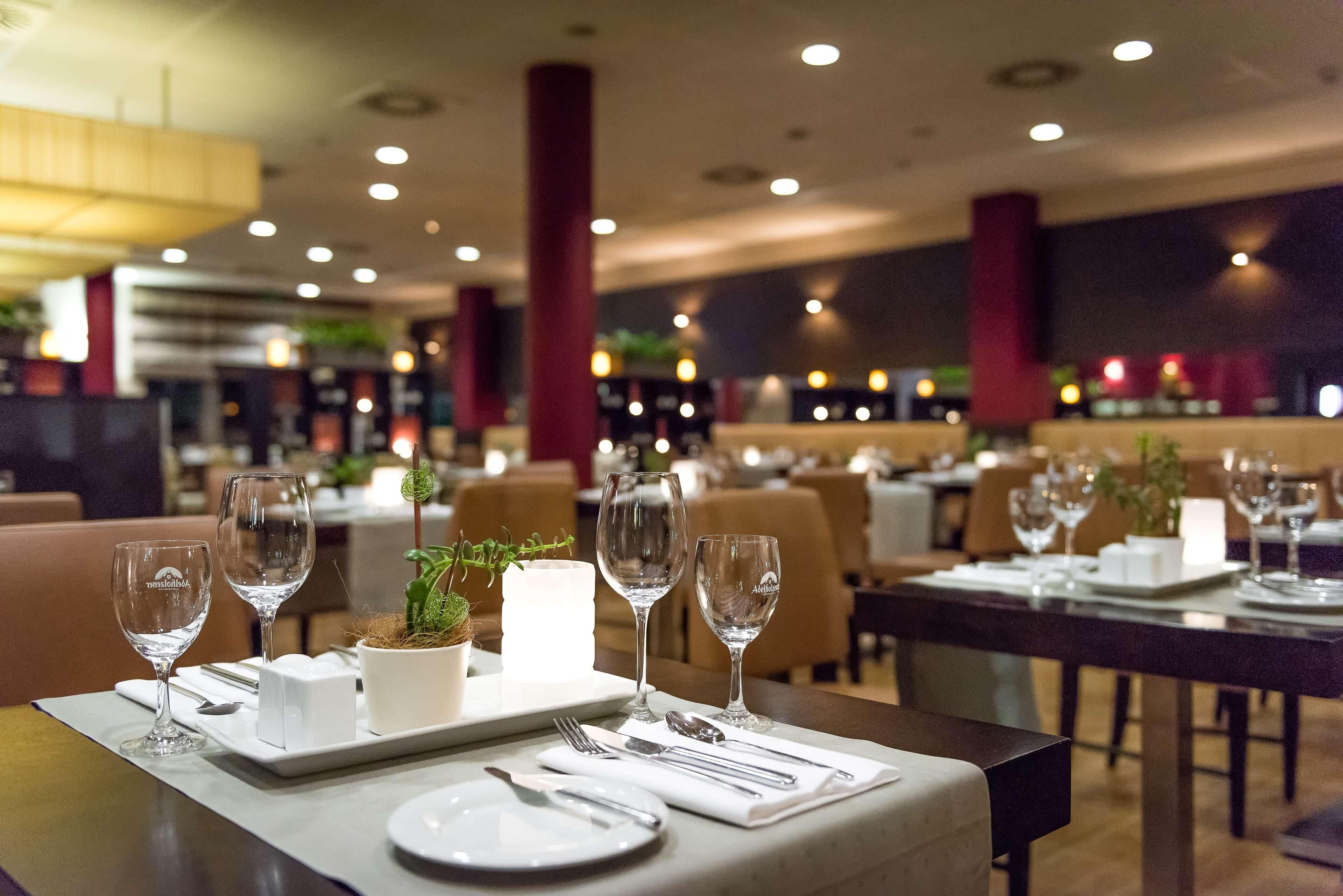 Interior de un restaurante con mesas listas para comer, destacando vasos transparentes y un centro de mesa con planta en maceta.
