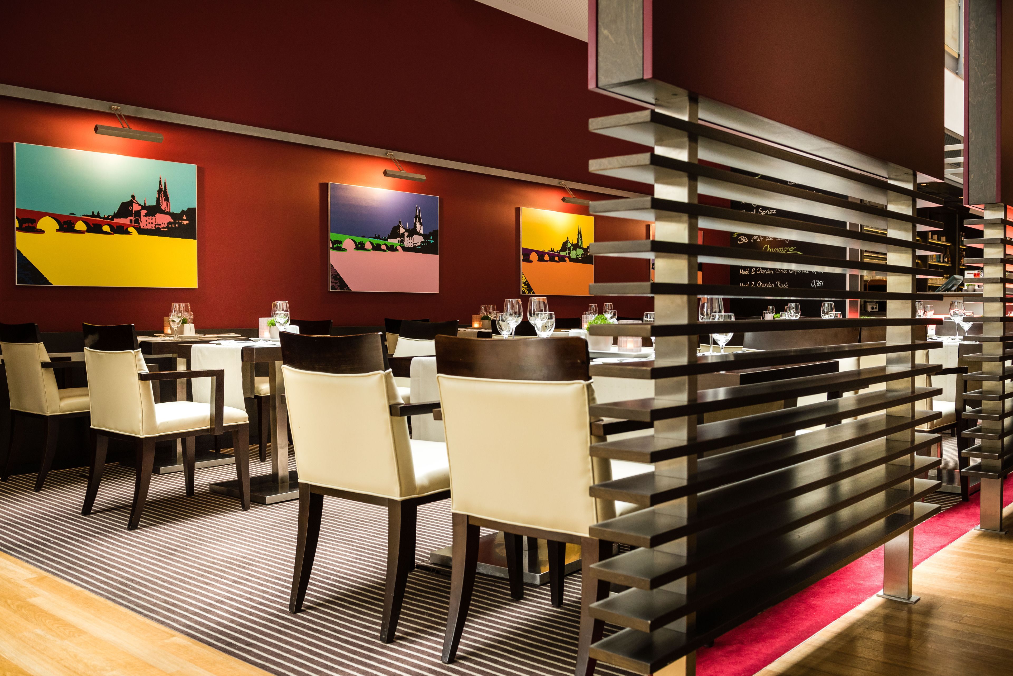 A restaurant with tables and chairs, a striped carpet, and artwork on the walls.