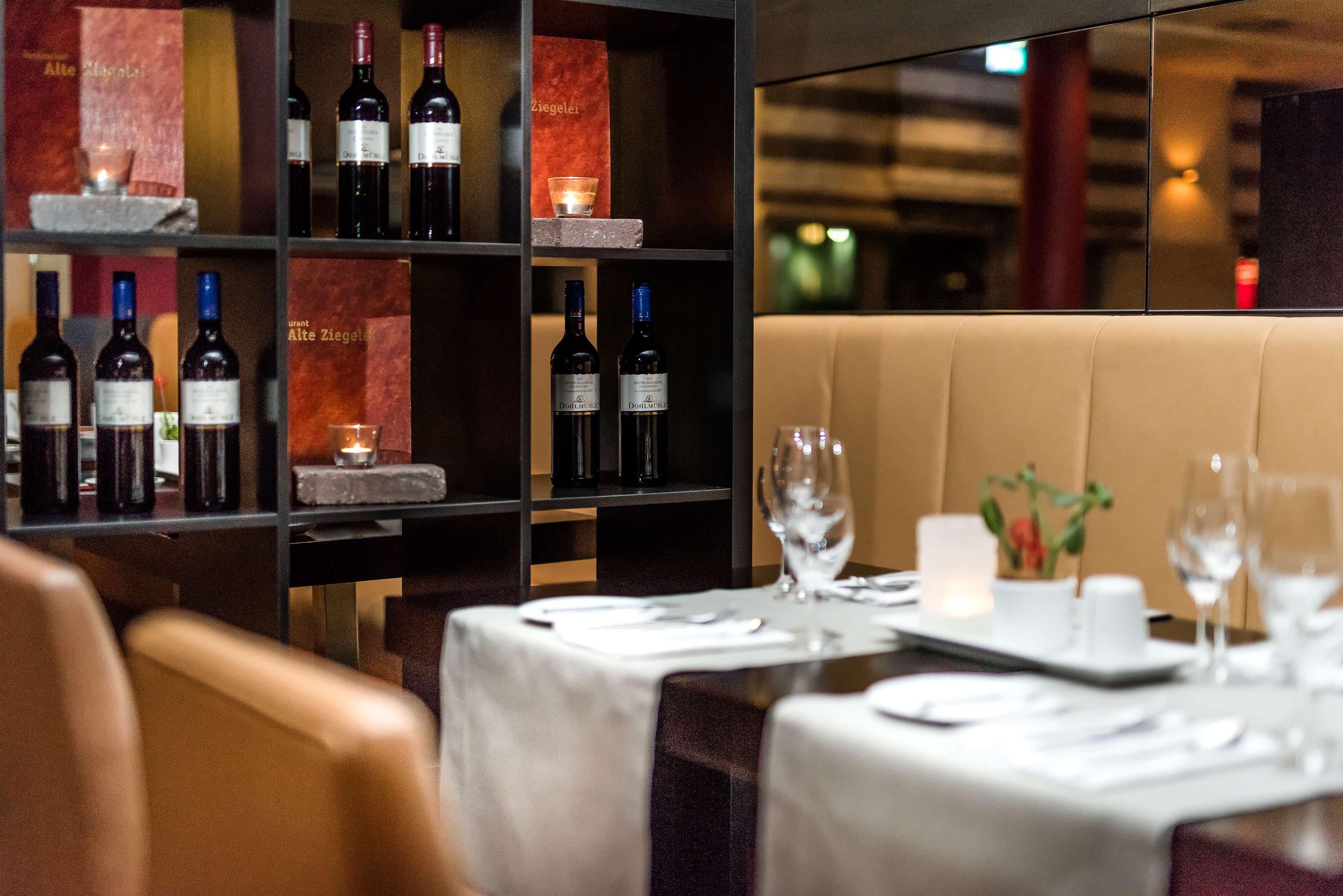 Ein Restaurantinneres mit einem für zwei Personen gedeckten Esstisch, einem Weinkühlschrank mit Flaschen und einer gemütlichen Sitzecke.